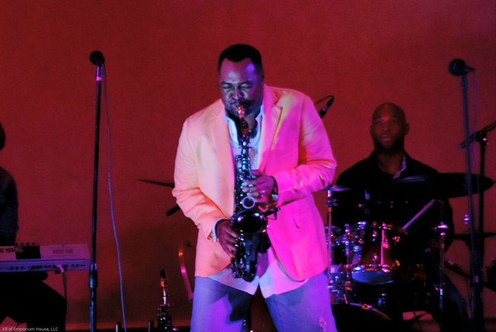 Saxophonist performing with a drummer under red stage lights